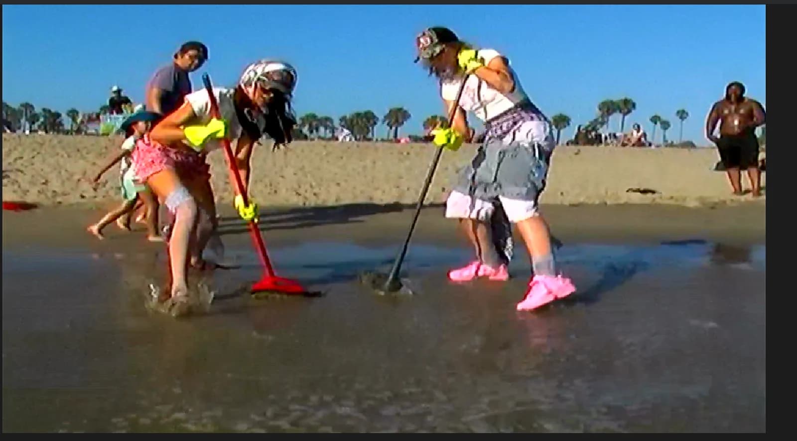 The two girls sweeping the beach in pink shoes and green gloves
