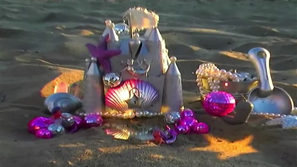 A sandcastle decorated with colorful shells, pearls, and shiny pink treasures