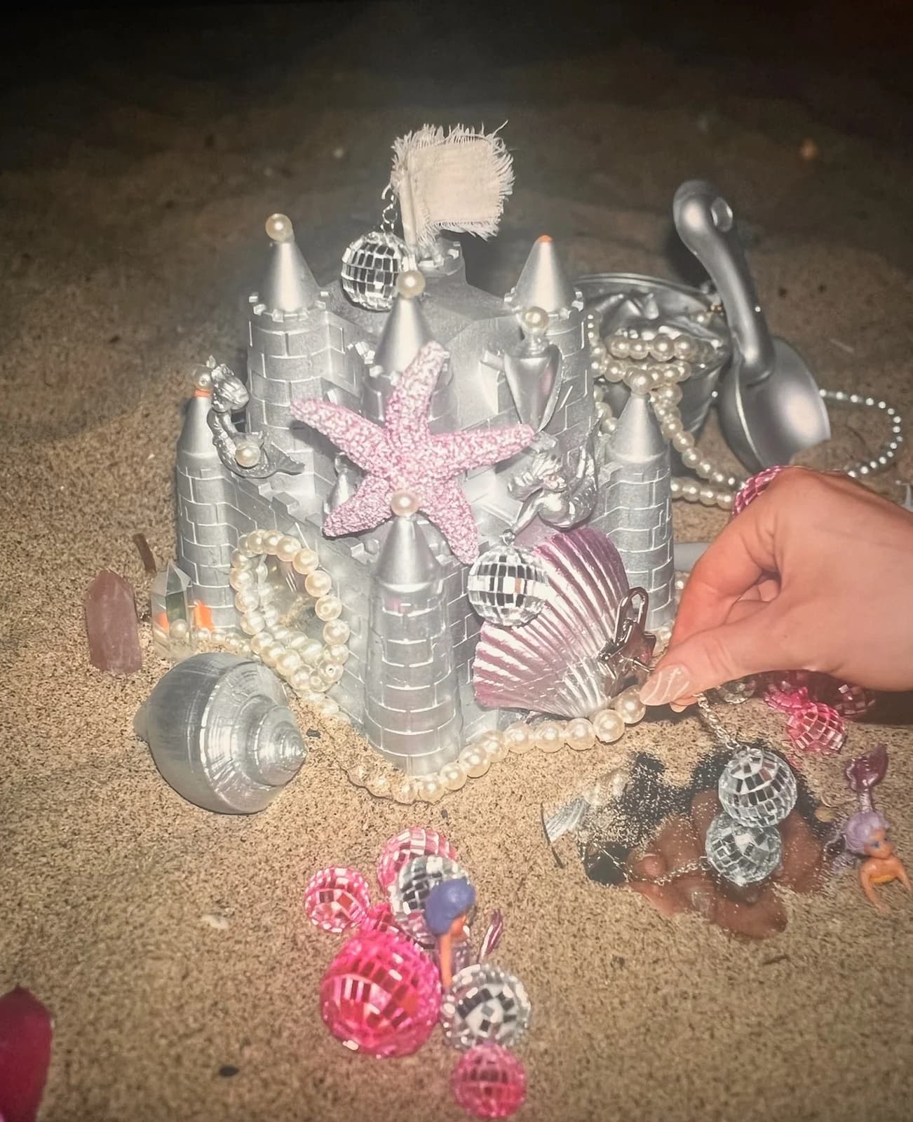 A silver beach castle decorated with pearls, shells, and pink disco balls